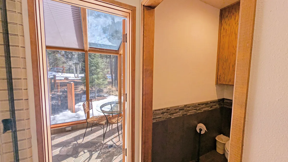 This image displays a view of a doorway that leads out to an outdoor seating area, blending cozy indoor elements like decorative tiles and wooden accents with glimpses of nature beyond. The ambiance is tranquil and relaxed, evoking the idea of unwinding with your pet after a day outside.