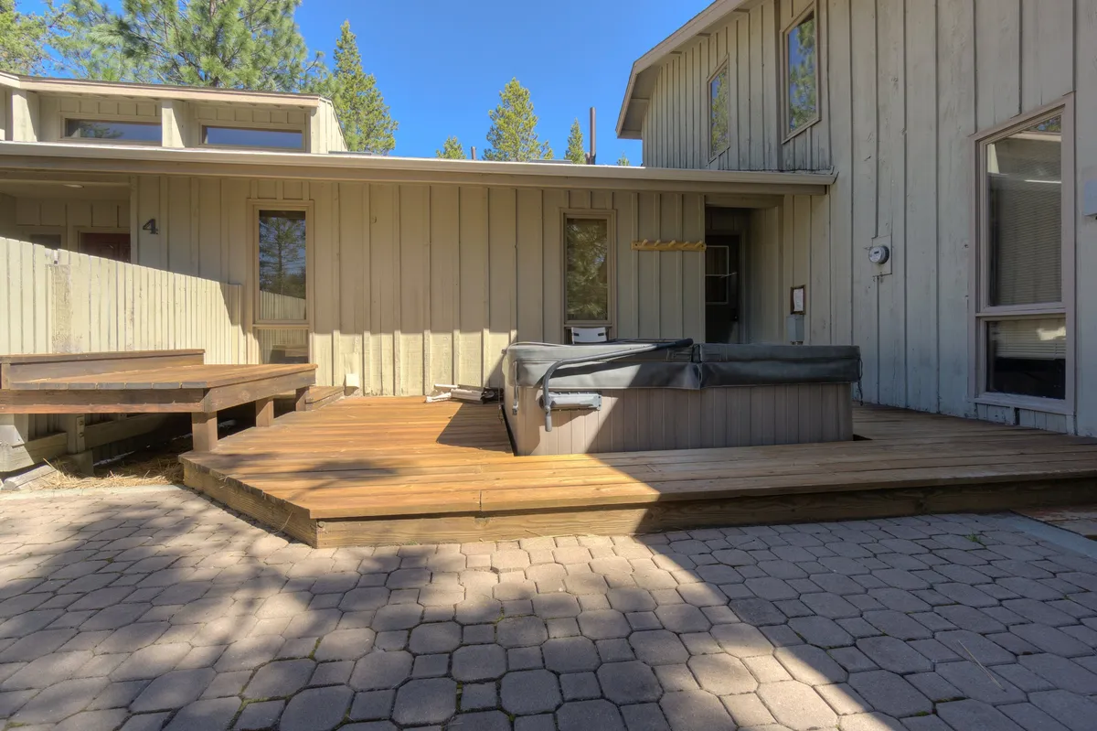 A wooden deck surrounded by pine trees, featuring a bubbling hot tub as the focal point. The setting is tranquil, offering privacy and a connection to nature, perfect for stargazing or relaxing after a long day.