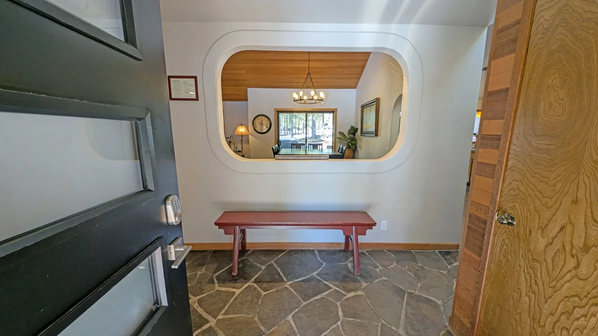 The scene captures an arched opening leading into a cozy interior, with a bench, stylish lighting, and sunlight streaming through a window. The image conveys a warm welcome and the sense of natural light central to eco-conscious living.