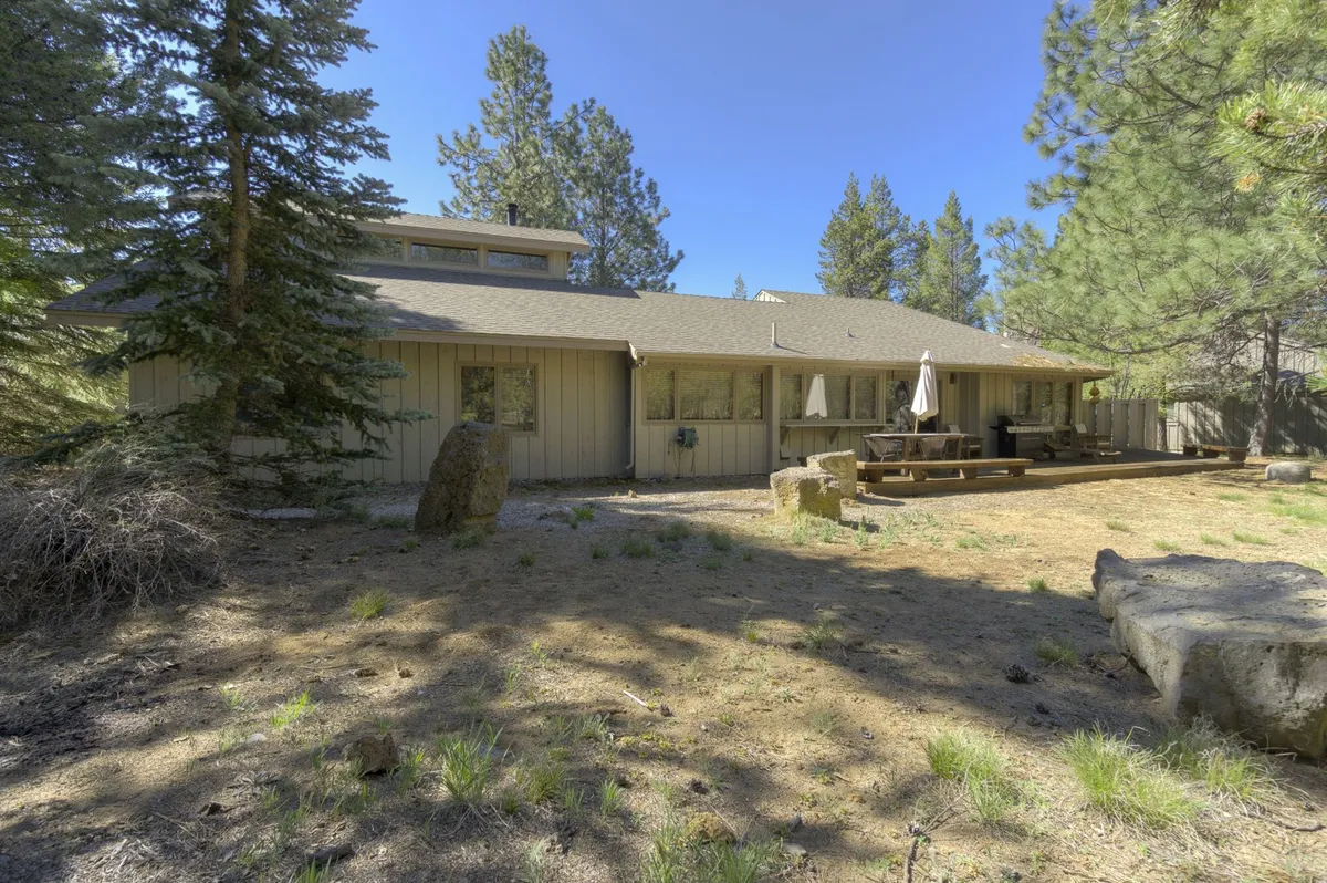 The wooden patio is nestled among large rock formations and trees, providing a serene setting for outdoor activities like barbecuing, dining, or simply absorbing the natural beauty. The sense of privacy and connection to nature is palpable.