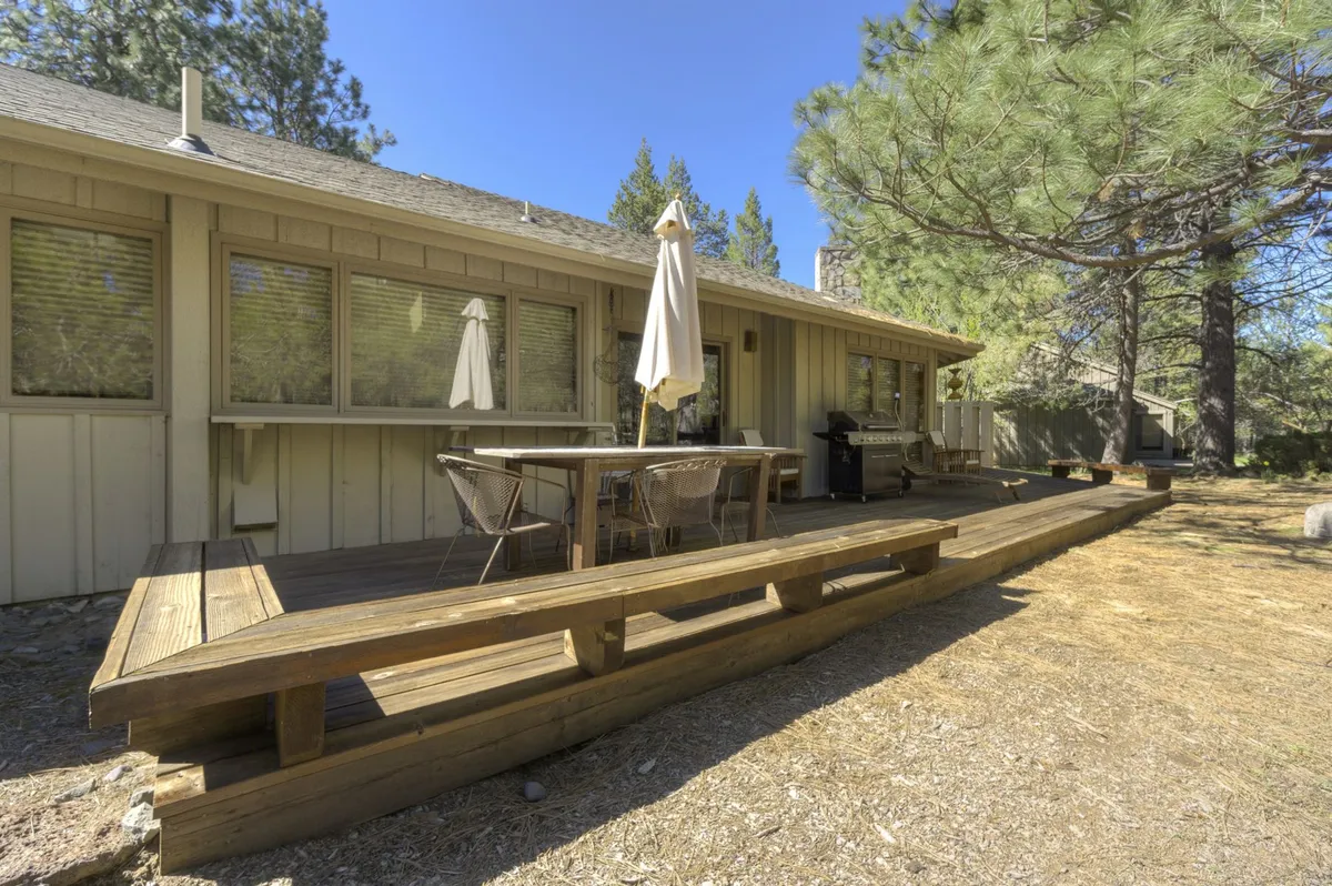 This image depicts a spacious deck with a table and chairs, grill, and umbrella, all set against a backdrop of trees. It captures the essence of outdoor living, with amenities for dining, relaxing, and enjoying the natural environment.