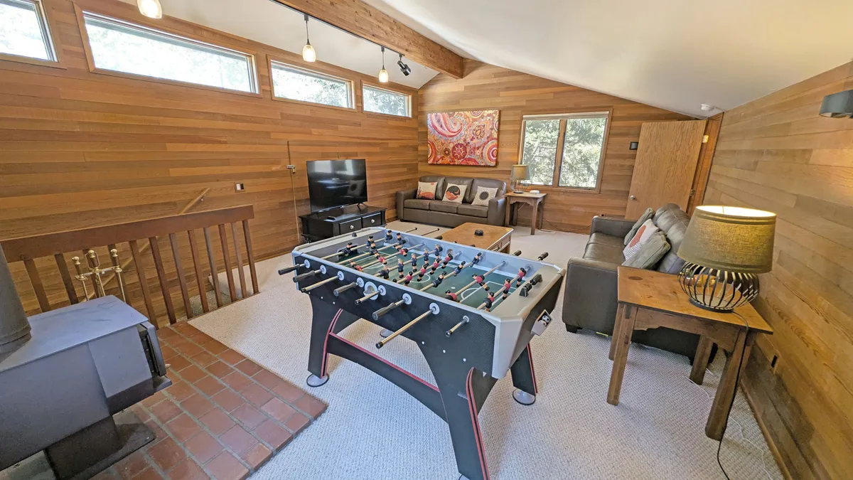 A cozy, playful living area featuring a foosball table, sofa set, TV, and wall art. The area is arranged for both recreation and relaxation, offering a space for game nights, streaming entertainment, or unwinding after outdoor activity. The mix of seating and playful elements supports a multifunctional atmosphere.