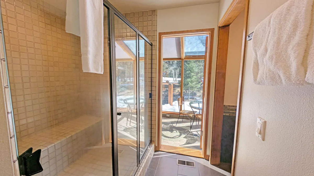 A modern bathroom with a glass shower enclosure, a large window letting in natural light, and a towel rack. The ambiance is tranquil, offering a sense of relaxation and rejuvenation.