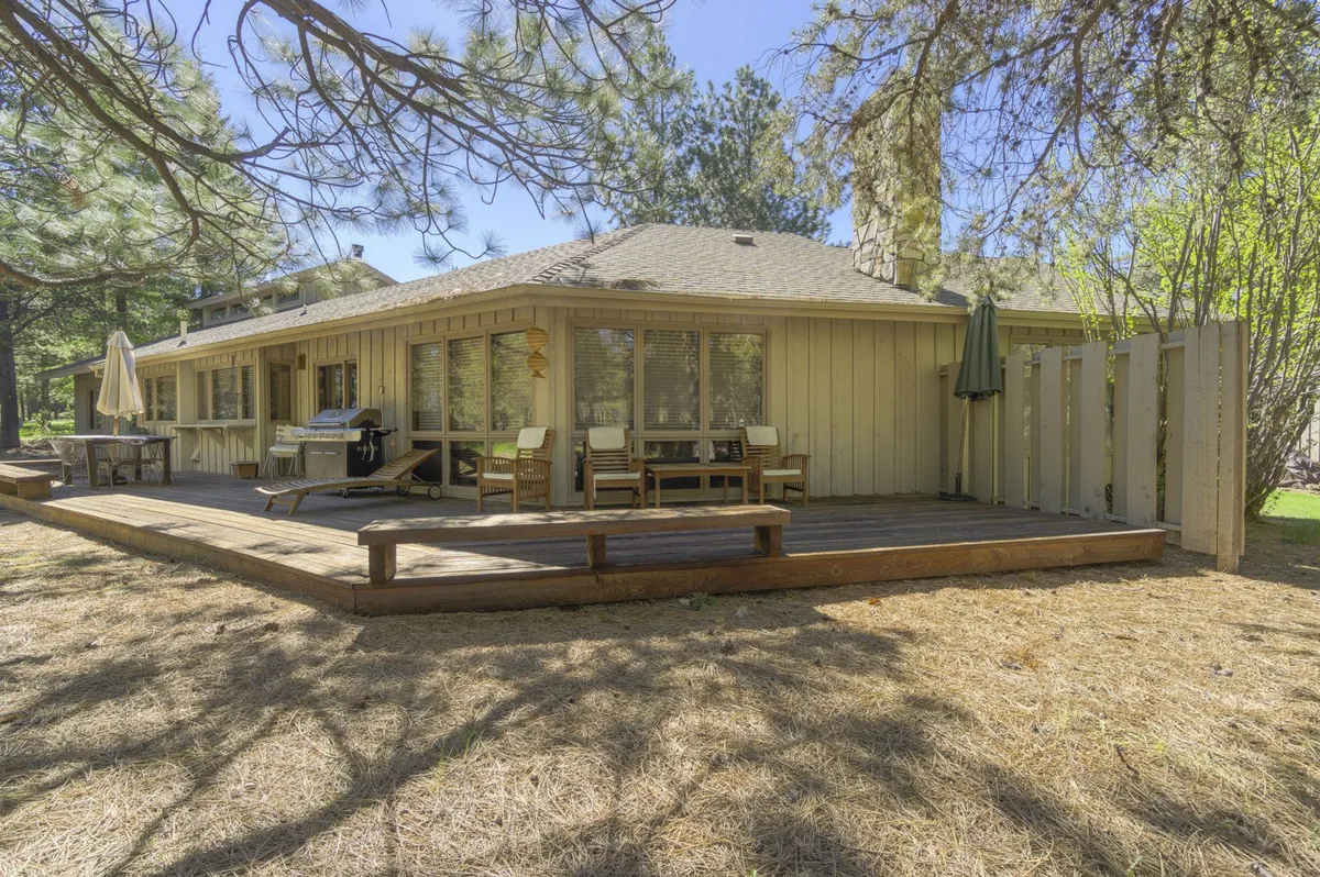 This image features a wooden deck with an outdoor seating area surrounded by mature trees, creating a tranquil outdoor living space perfect for relaxing or entertaining. The natural setting is visible, evoking the inviting transition from indoor comfort to outdoor recreation.
