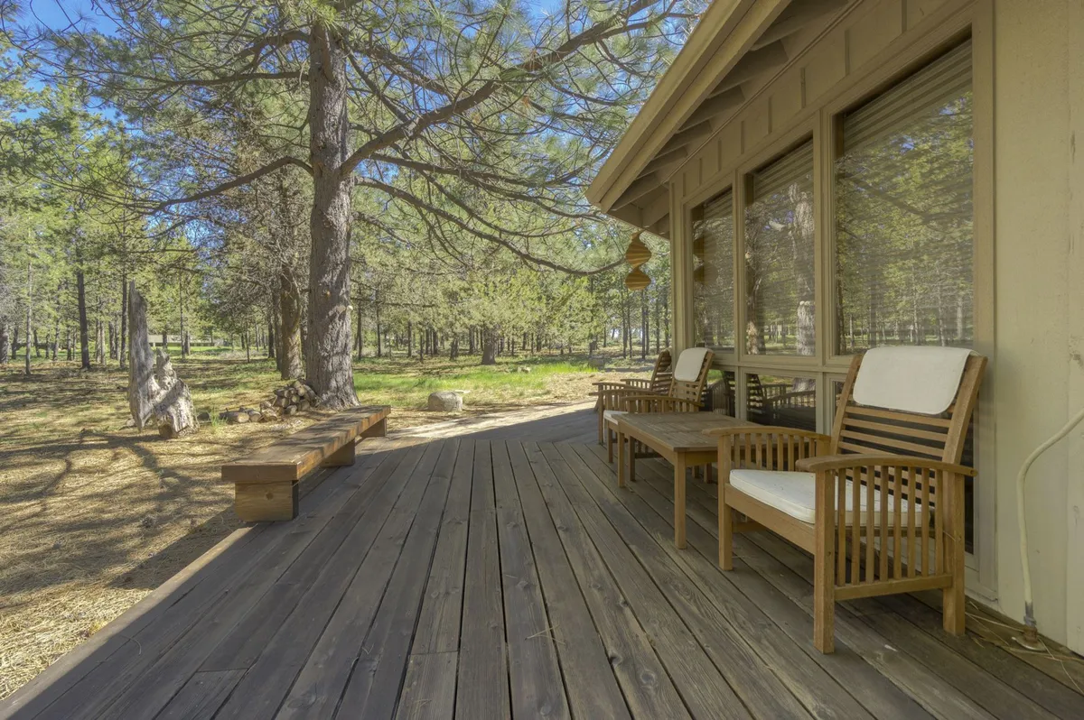 An expansive wooden deck with comfortable outdoor seating is surrounded by tall trees. The deck is bathed in natural light, offering views of the forest and a quiet, peaceful atmosphere. This outdoor space feels like a private haven, blurring the line between indoor comfort and the natural world just steps away.