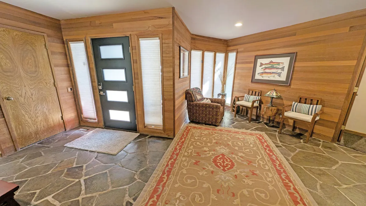 This image shows the front door area of the home, with a comfortable seating space, a stylish rug, and welcoming artwork. The scene captures the transition between inside and outside, suggesting easy access to Sunriver adventures right from the doorstep. The mood is inviting and cozy, hinting at the pet-friendly hospitality of the property.